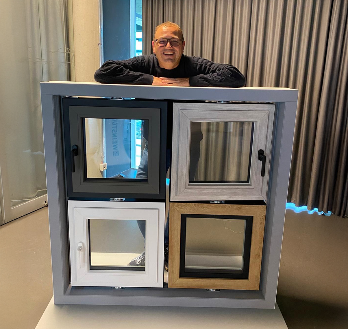Markus Lieber 2025 in seinem Showroom Mann hinter einem Fensterdisplay mit verschiedenen Rahmenarten in Schwarz, Weiß, Grau und Holzoptik in modernem Showroom.