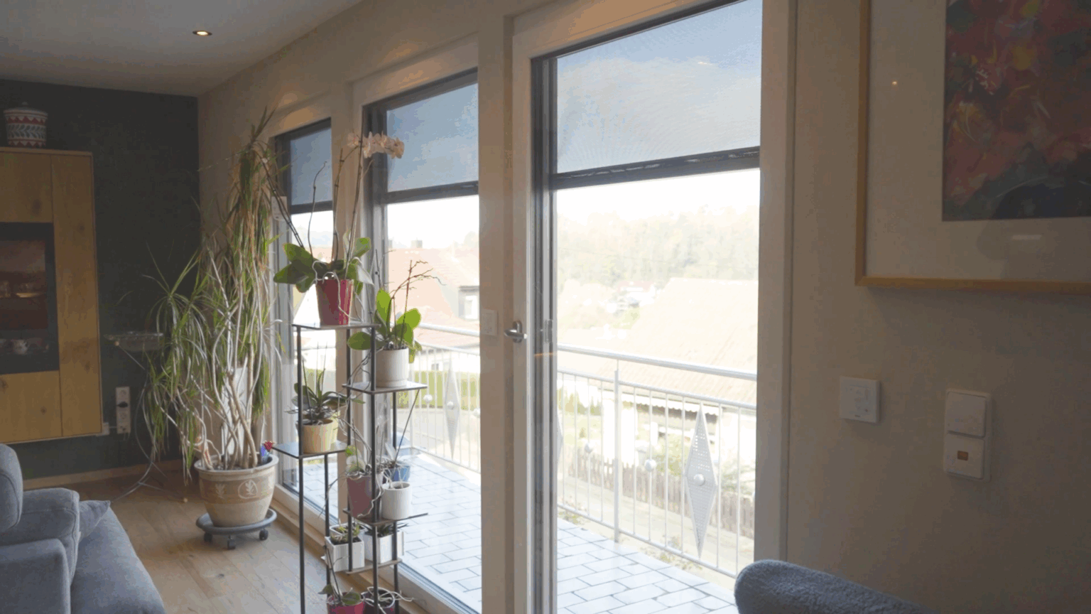 Fenster-12 Wohnzimmer mit großen Fenstern, lichtdurchflutet, Zimmerpflanzen und Balkonblick.