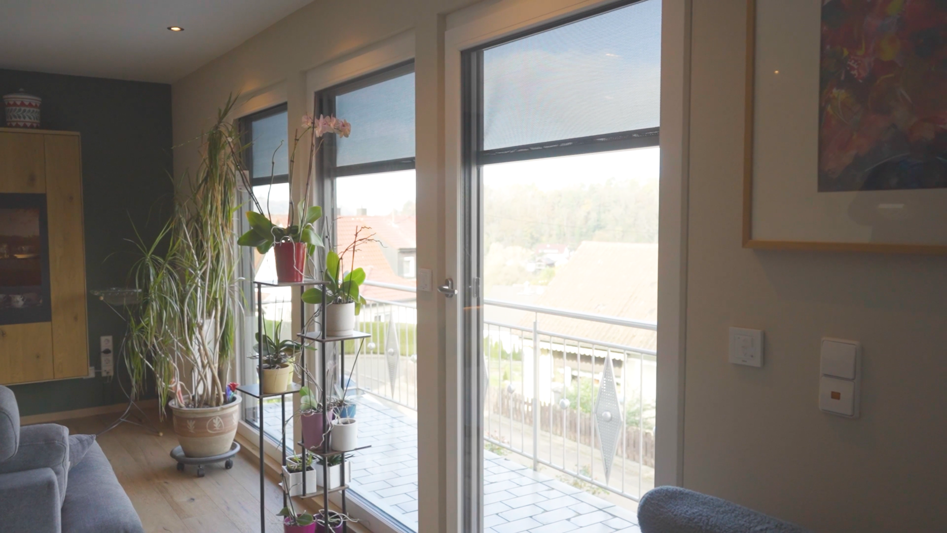 Fenster-12 Wohnzimmer mit großen Fenstern, lichtdurchflutet, Zimmerpflanzen und Balkonblick.